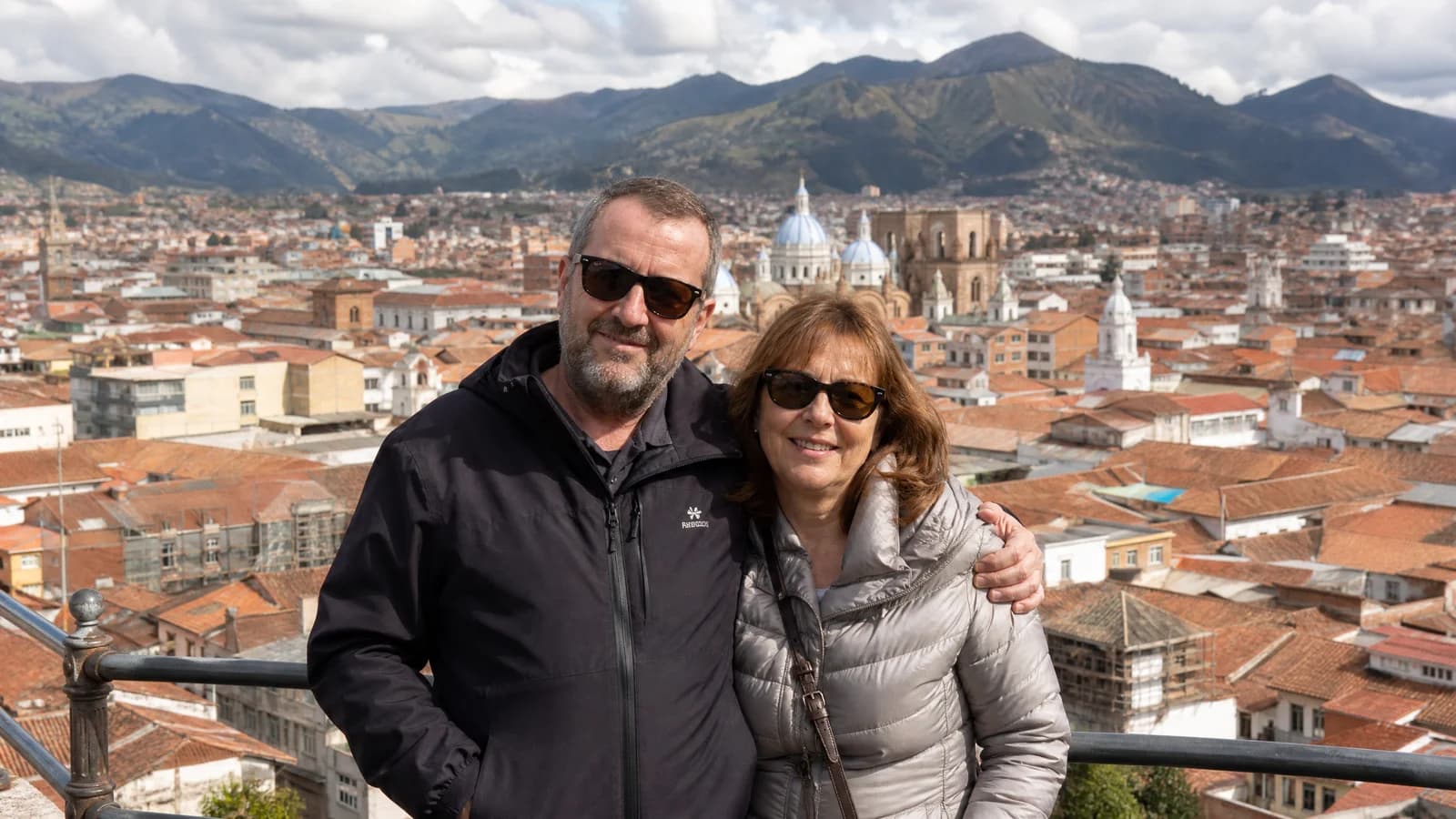 Paar auf einem Aussichtspunkt ueber der Kolonialaltstadt von Cuenca mit roten Ziegeldaechern und Andenkulisse im Hintergrund.