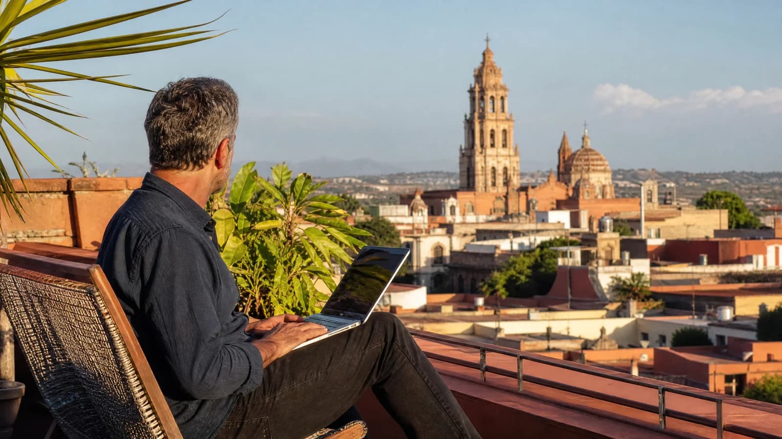 Auswanderer auf einer Dachterrasse in einer mexikanischen Kolonialstadt mit Laptop und Blick ueber Terrakottadaecher.